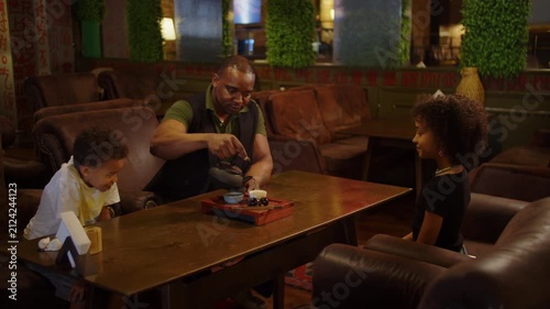 Father pouring tea for children during family tea time in cafe