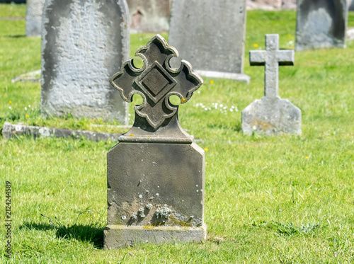 Close and selective focus on an ornate headstone in a cemetery, with soft bokeh and blurred background, emphasizing stone detail and a quiet, reflective atmosphere.