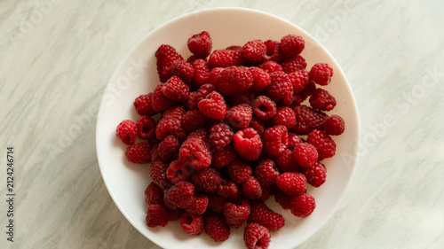 Extreme close-up of fresh red raspberries in a white bowl under warm natural sunlight.
