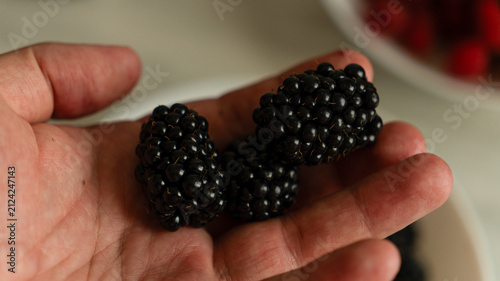 Fresh blackberries in a white bowl on a marble counter with raspberries blurred in the background.