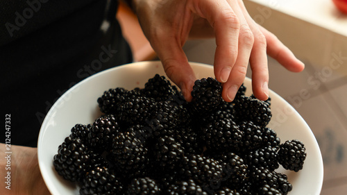 Fresh blackberries in a white bowl on a marble counter with raspberries blurred in the background.