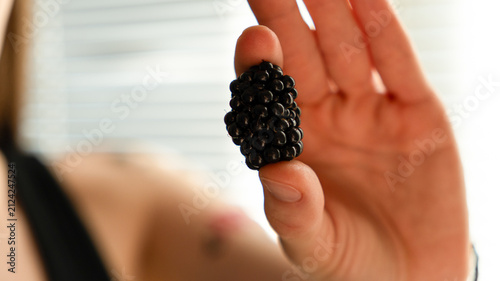 Close-up of hands holding a white ceramic bowl filled with fresh black ripe blackberries.
