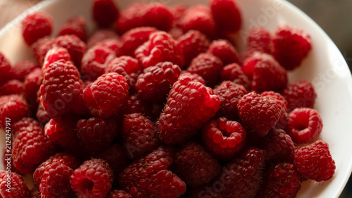Extreme close-up of fresh red raspberries in a white bowl under warm natural sunlight.