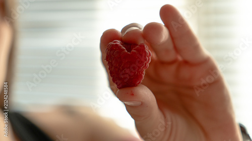 Extreme close-up of fresh red raspberries in a white bowl under warm natural sunlight.