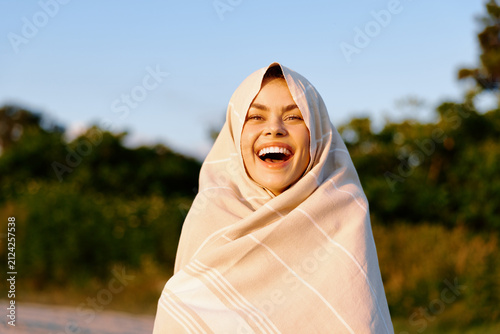 Bild auf Leinwand Radiant young woman wrapped in a light shawl laughs with her head tilted back under bright sun, expressing carefree summer joy in an outdoor setting