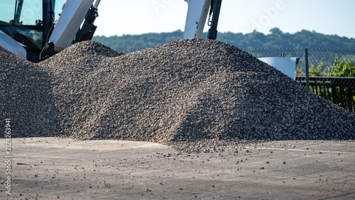 Fotografie massive pile of gray crushed stone gravel at an active outdoor construction site with excavator in the background on a bridge area