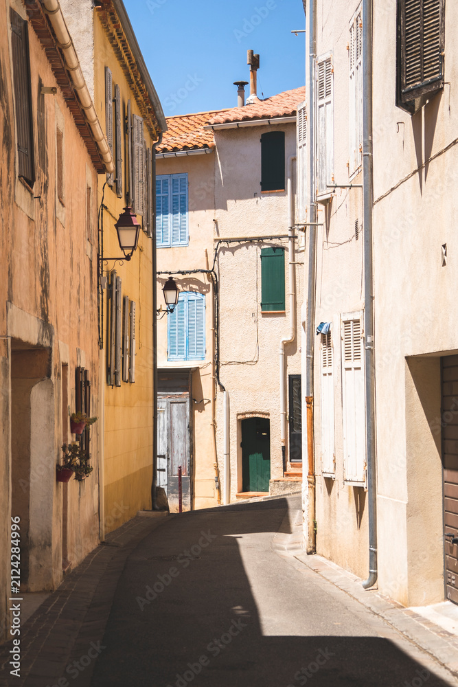 Fototapeta premium A gentle curve in a narrow European alleyway reveals historic multi-story buildings painted in warm pastel hues. Colorful wooden shutters in blue and green contrast against the sunny facade, evoking c