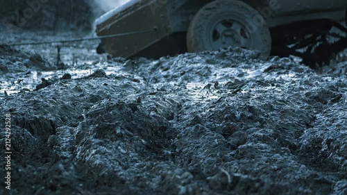Low angle close up of thick, wet mud churned by off road vehicle. SUV in background with tow cable. Cool, blue tones create gritty, adventurous mood for extreme sports or challenge concepts