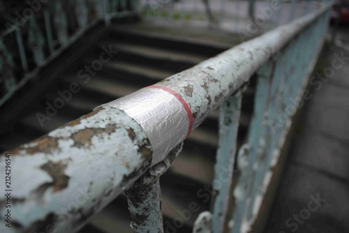 Rusty railing on a staircase with tape wrapped around it in a city setting during the day