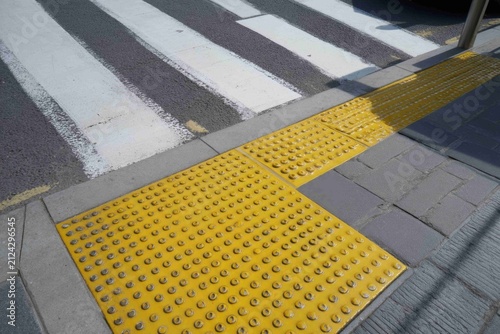 Sidewalk with crosswalk markings and tactile paving located in a busy urban area during daytime