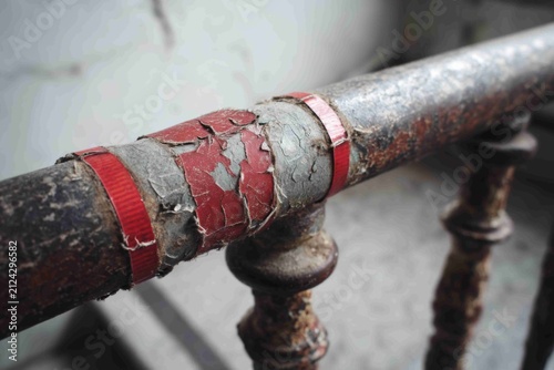 Rusty metal railing shows wear and damage inside an old building with peeling paint and visible signs of age