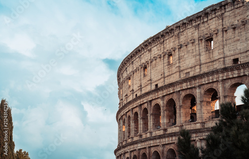 Colosseum, an iconic ancient Roman amphitheater, stands against a bright blue sky filled with white clouds, showcasing its historic architecture and enduring legacy as a symbol of the Roman Empire
