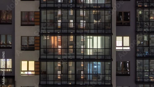 facade of a modern apartment building at night, lights on in the windows, panorama down