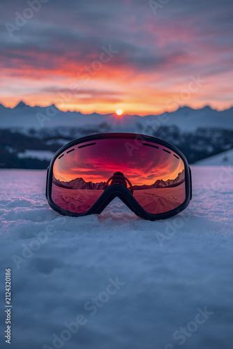 Ski goggles on fresh snow reflecting mountain sunset