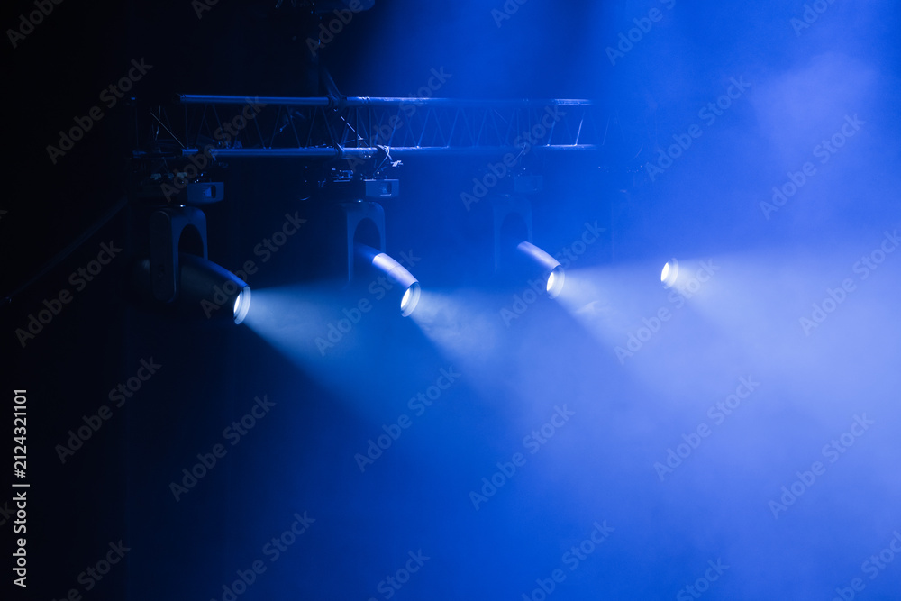 Naklejka premium Powerful blue spotlights pierce thick fog on a dark stage, creating a moody theatrical atmosphere ideal for concerts, performances, events, and promotional visuals that highlight lighting design