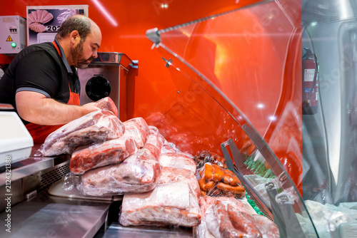 Butcher arranging packaged meat in refrigerated display case
