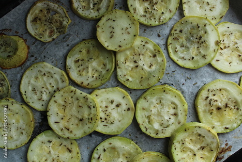 Sliced zucchini rounds seasoned with herbs and oil on parchment paper, capturing a top-down view of healthy food preparation and roasting.