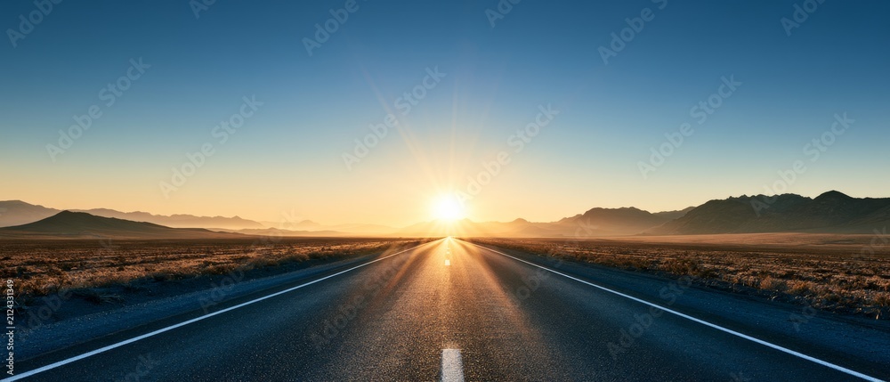 Obraz premium Sunrise over a long straight road in a wide open landscape with mountains in the background