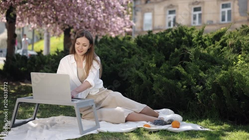 Laptop Work, Female Freelancer, Park Computing. In tranquility of sakura-clad park, woman diligently works on her laptop.
