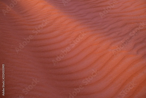 texture of deep red sand ripples with soft curves under warm low twilight evening light in the Sahara desert of Erg Chebbi near Merzouga Morocco