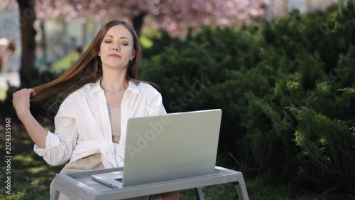 Park Computing, Working Laptop, Nature Office. Under sakura trees in park, woman is absorbed in her laptop work.