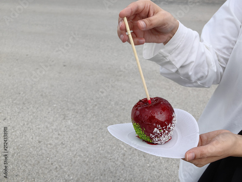 Cuadro en lienzo Hands holding a glazed candied apple on a white paper plate with a wooden stick