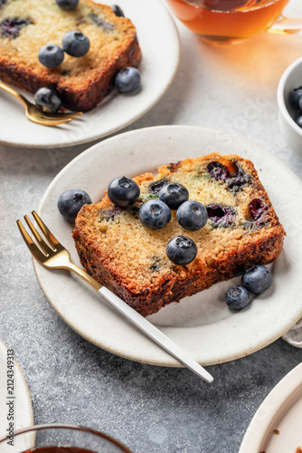 Zucchini blueberry bread sliced served on ceramic plate with tea. Moist cake with grated zucchini and fresh berries on gray textured background