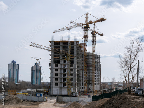 Construction site with tower cranes and high-rise building under development against a clear sky, urban architecture and building industry