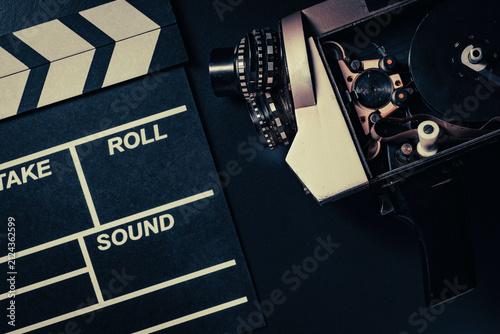 Vintage movie camera and clapperboard on black background, closeup. Top view of an open retro movie camera with film reel next to black movie clapperboard on dark surface