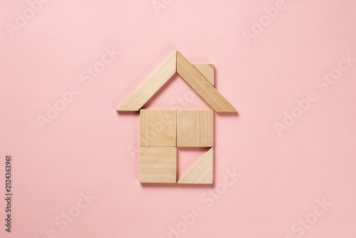 Conceptual house structure formed by natural wooden blocks on a soft pink background, symbolizing home ownership, construction, property investment, and secure living spaces