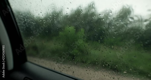 Close up of rain drops on car window during forest road trip with audio included