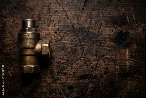 Vintage heavy brass industrial thermostatic valve element on dark wooden workbench with copy space