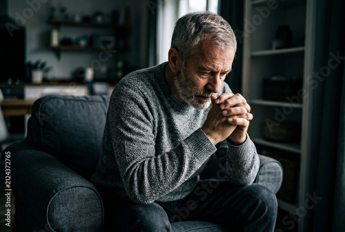 Thoughtful senior man sitting alone on armchair at home