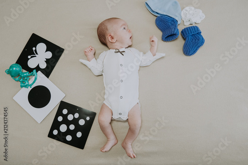 Cute 1 month baby boy lying among various playful colorful toys on beige blanket. Newborn surrounded by vivid objects participating actively in sensory exploration and learning. 