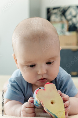 Baby boy lying on bed and gripping teething ring with both hands. Child chewing toy for teething relief. Exploring textures while soothing sore gums. Sensory discovery at home 