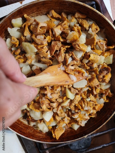 Chanterelle mushrooms, potato and onion frying in a pan while a female hand stirs with a wooden spatula,recipe,taste.Russia,Luga