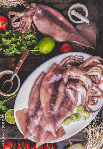 фотографія Fresh raw seafood squid or calamary and ingredients on dark background