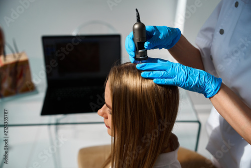 Medical trichologist uses a digital dermatoscope in a clinic to execute a precise scalp examination and root analysis.