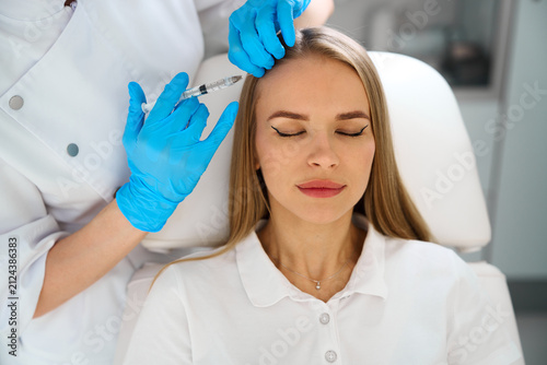 Detailed shot of a doctor in blue gloves performing a scalp injection on a female patient during a hair restoration session.
