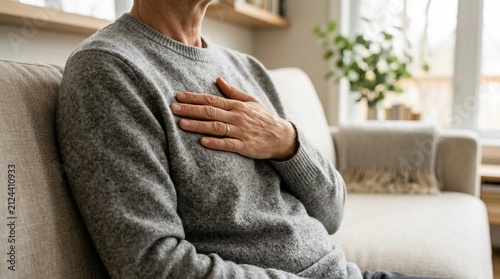 Senior man feeling chest pain while sitting on the sofa at home indicating heart health concerns and cardiovascular discomfort