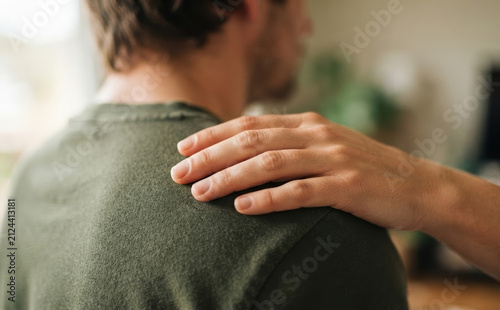 Young adult man receiving comforting touch on shoulder from friend in supportive gesture