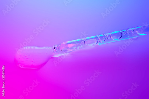 Cosmetic serum dropping from pipette onto vibrant background