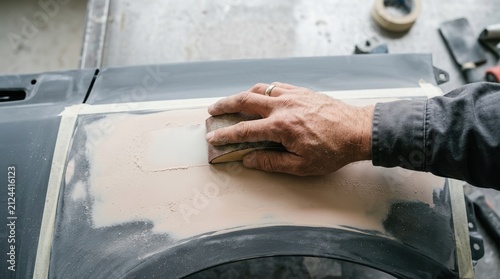 Skilled mechanic hand sanding car body filler with sandpaper for smooth auto repair
