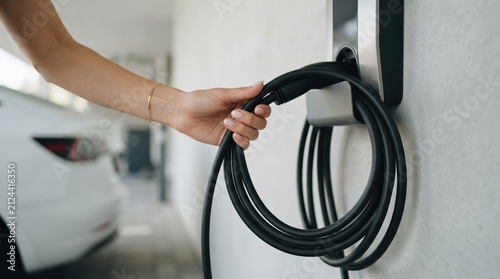Woman holding electric vehicle charging cable in garage to power her white car for sustainable travel