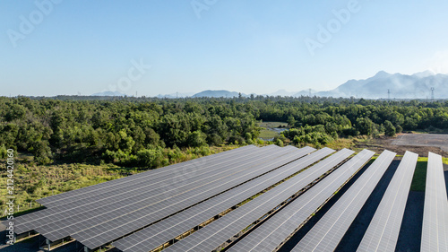 Large solar farm with rows of photovoltaic panels set against a backdrop of lush green forest and distant mountains in Itaguai, Rio de Janeiro, Brazil. Aerial view.