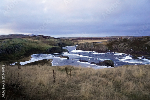 Konstfotografi An icy river winds through a rugged landscape of grassy hills and rocky bluffs u