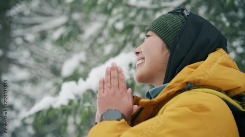 Woman in yellow jacket and green beanie praying in snowy forest during winter hike