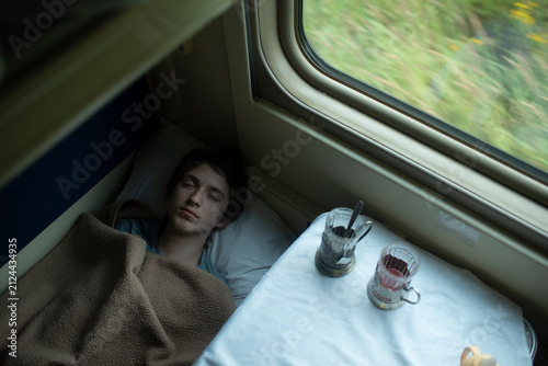 Teenage boy sleeping inside passenger train compartment on summer trip
