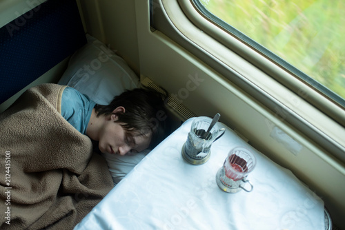 Teenage boy sleeping inside passenger train compartment on summer trip