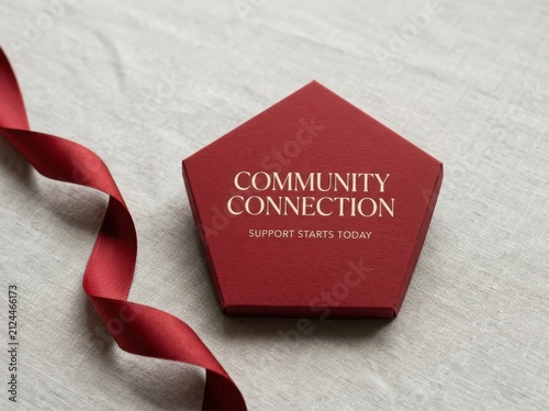 Elegant pentagonal red box with community connection text on grey textured fabric beside a silk ribbon representing social support programs and non profit organization branding for charity